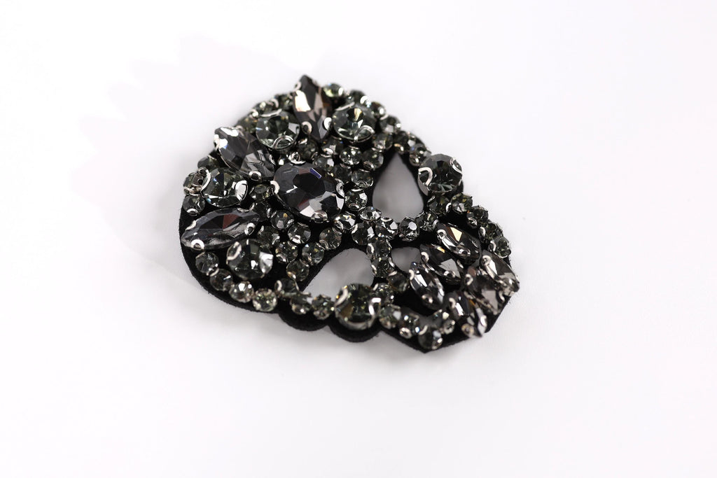 A close-up image of a black and silver rhinestone-encrusted object, possibly a brooch or a piece of jewelry, against a white background.
