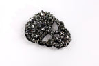 A close-up image of a black and silver rhinestone-encrusted object, possibly a brooch or a piece of jewelry, against a white background.