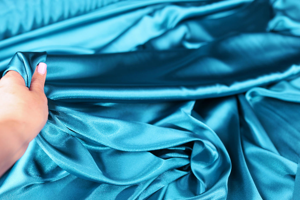 a woman&#39;s hand on a blue satin material