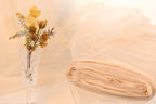 a clear glass vase holding a bouquet of yellow flowers, placed on a table with a white cloth draped over it.