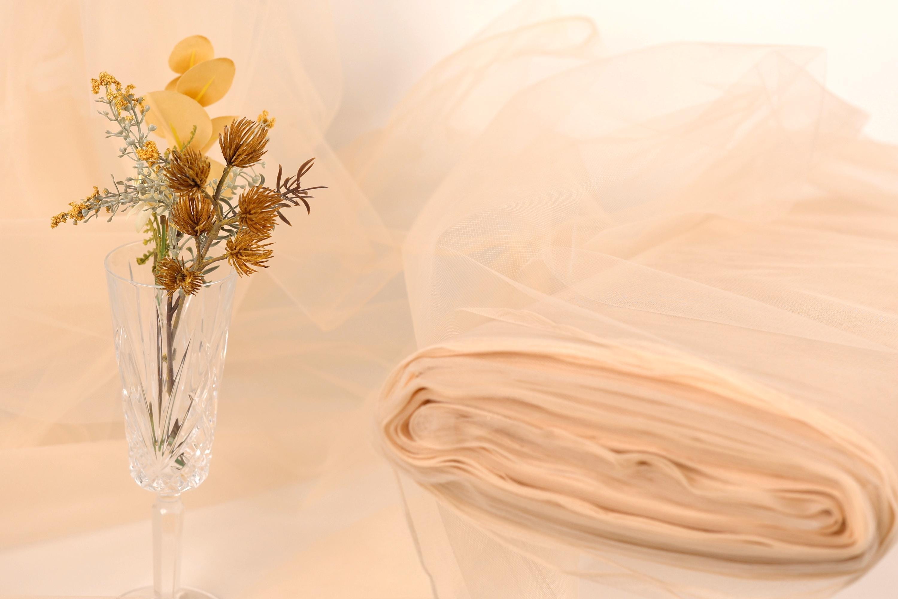 a clear glass vase holding a bouquet of yellow flowers, placed on a table with a white cloth draped over it.