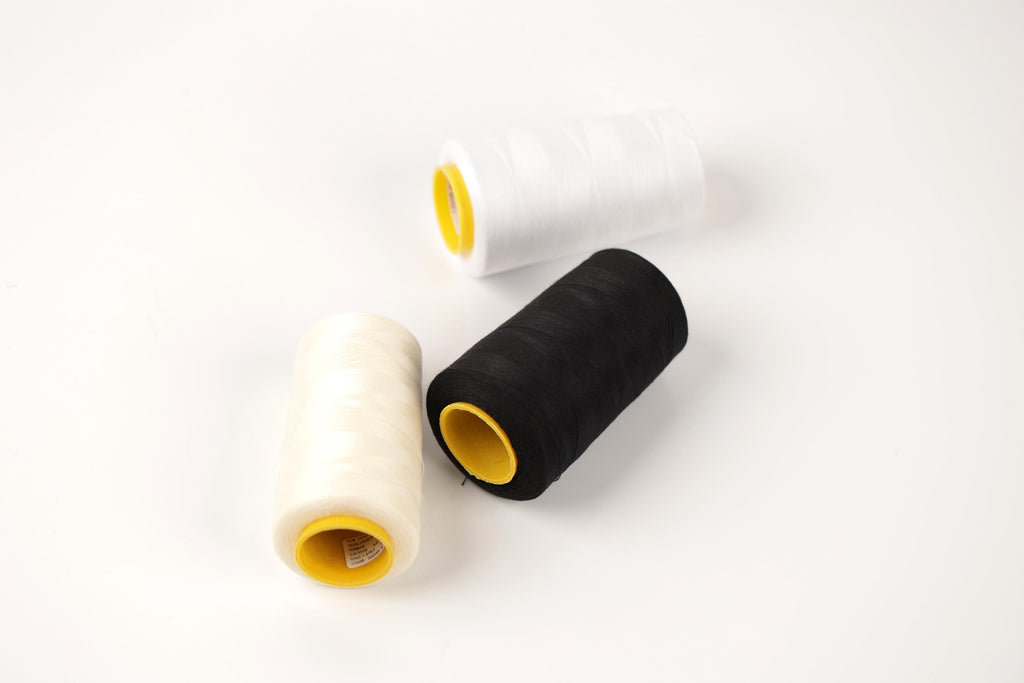 three spools of thread, two white and one black, arranged on a white background.