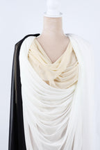 A mannequin wearing a white and beige draped garment with a black fabric draped over the left side.