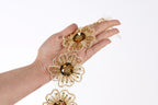 A hand holding a chain of gold-colored, intricately designed flowers against a white background.