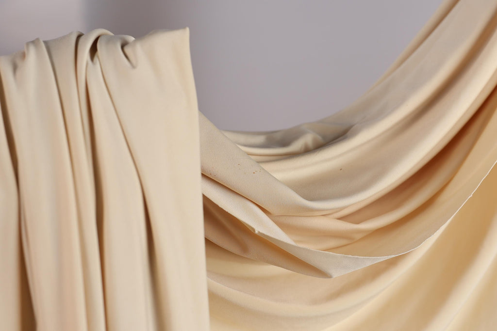 A close-up view of a beige fabric, possibly a curtain or drape, with a soft, flowing texture.