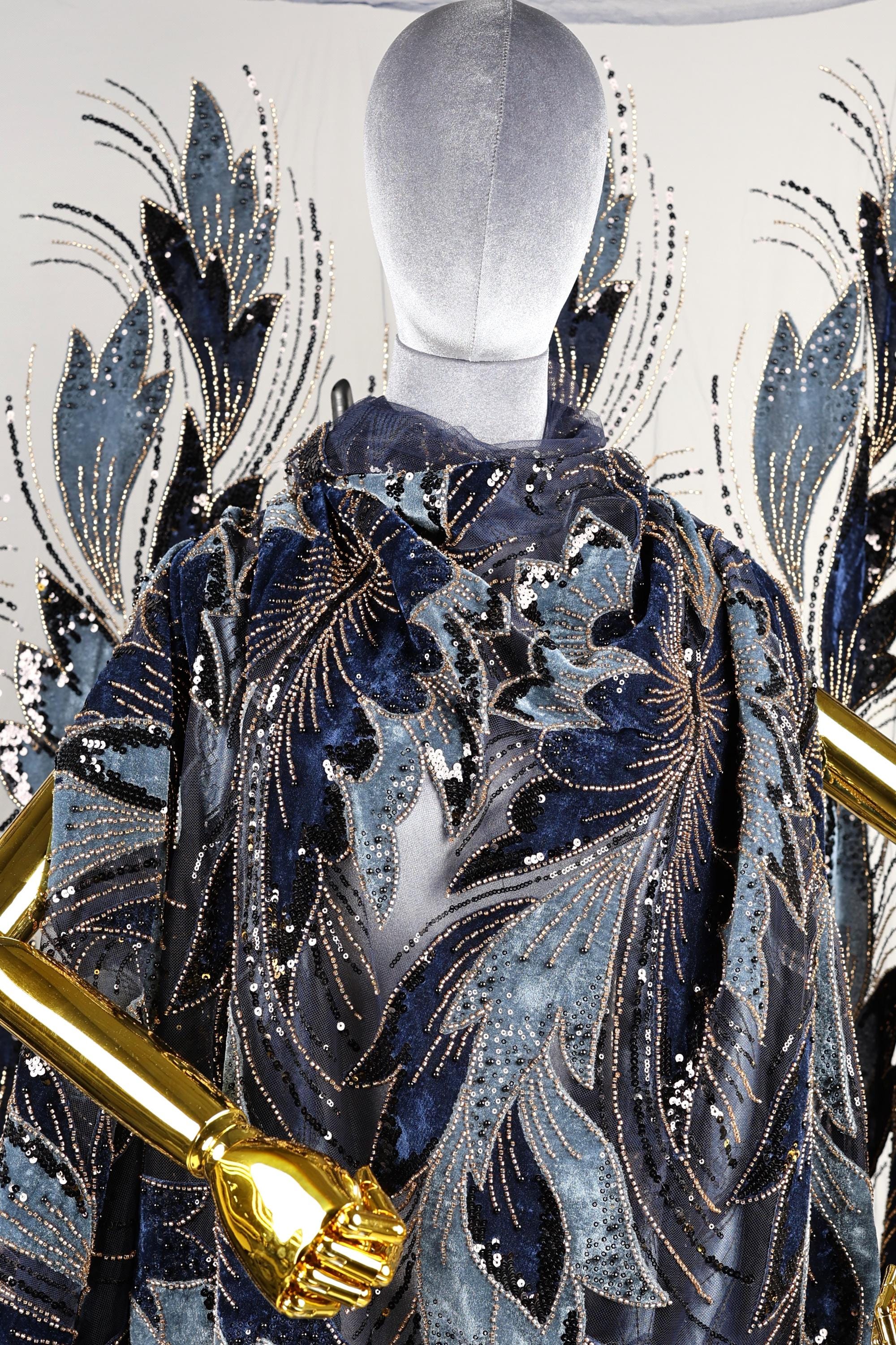 a mannequin wearing a blue and gold patterned cape with gold sequins and a gold metallic design.