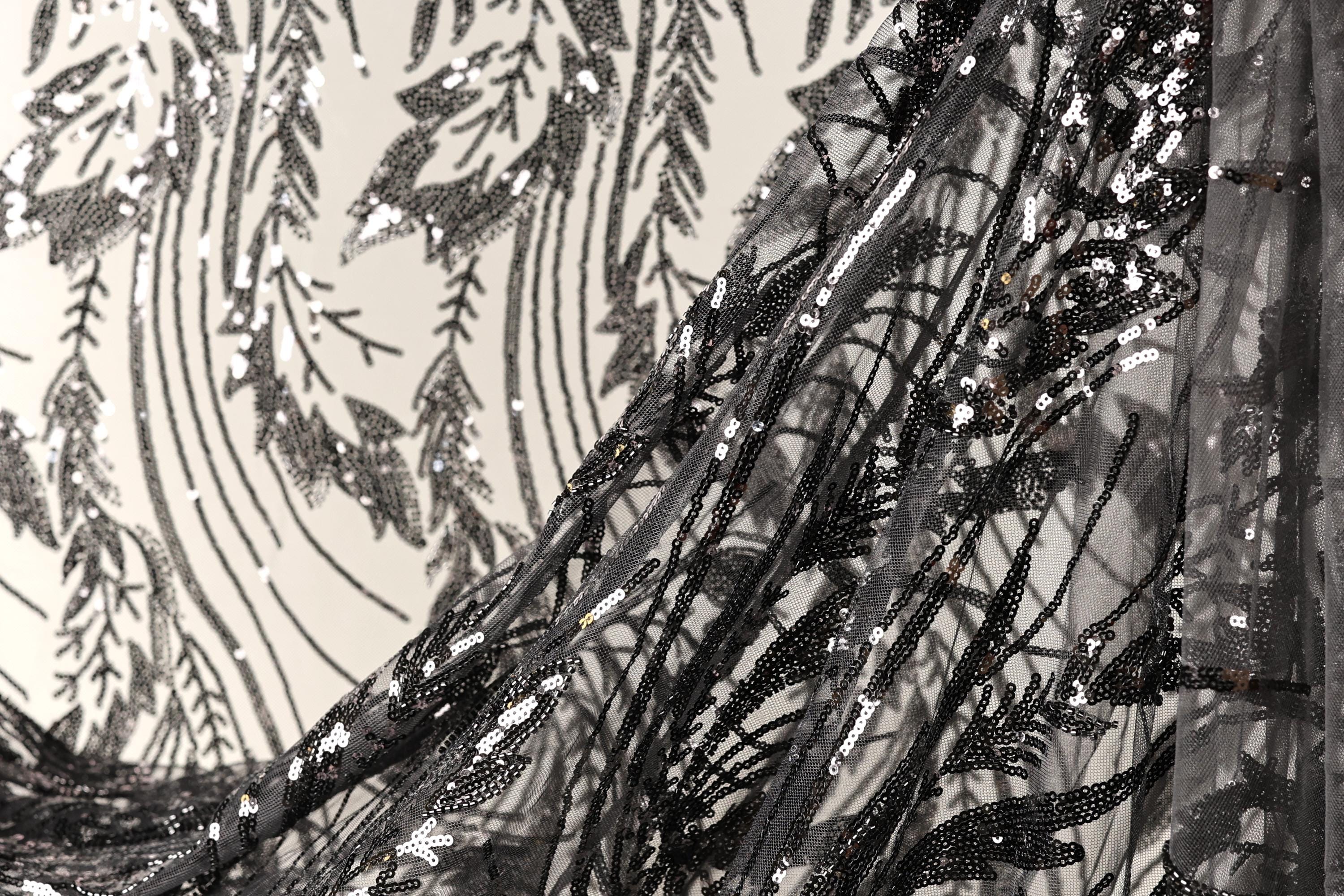a close-up view of a black and white fabric with intricate black and white sequin patterns. The fabric appears to be a sheer or sheer-like material, with a delicate and elegant design.