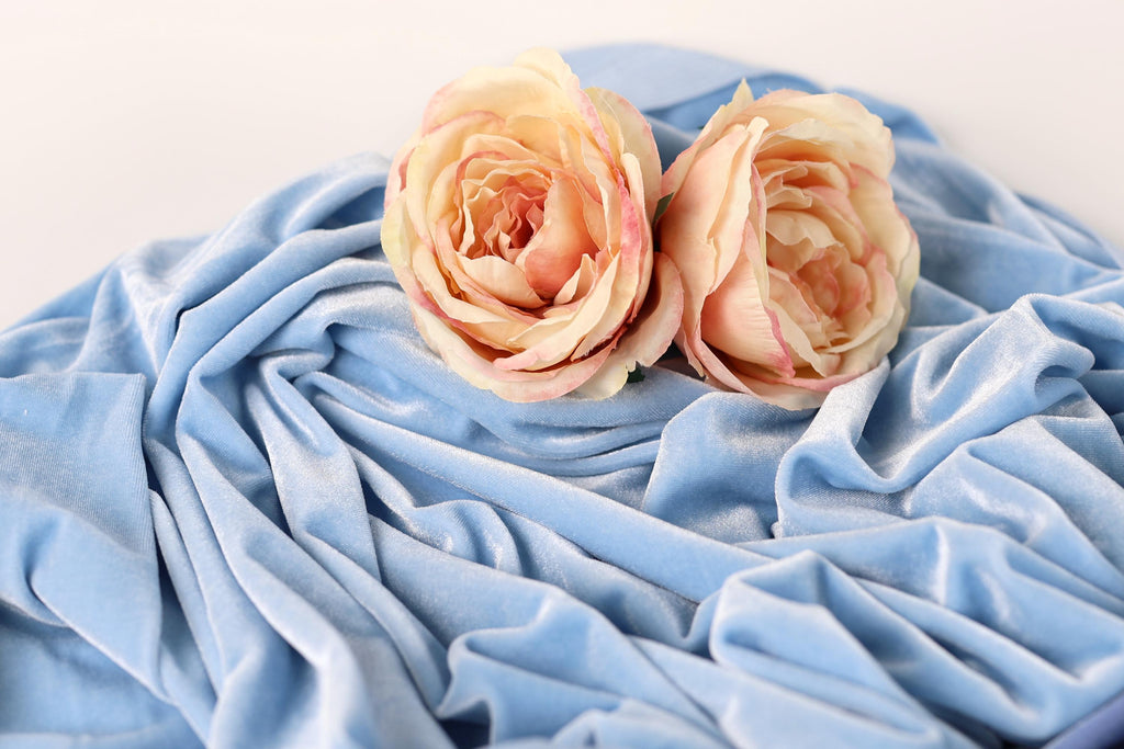Two delicate pink roses resting on a crumpled blue fabric.