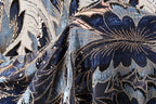 a close-up view of a fabric with a floral pattern, featuring a mix of blue, black, and gold colors. The fabric appears to be made of a shiny material, possibly sequin or beads, and has a textured appearance.