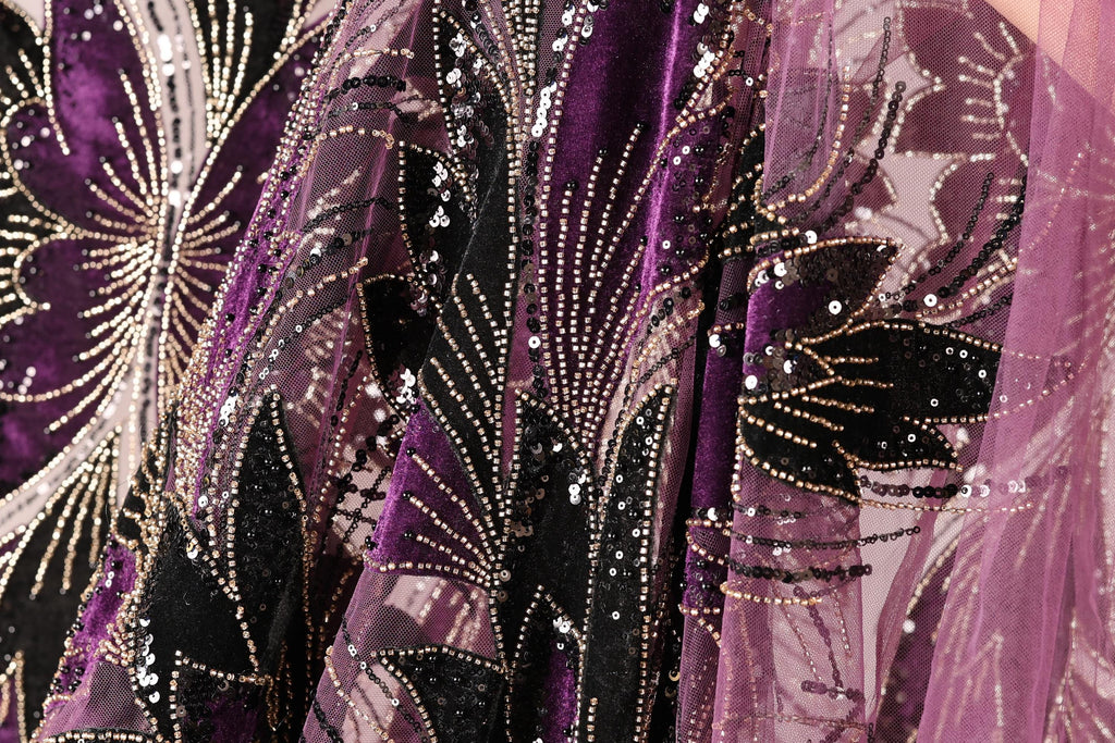 a close-up view of a fabric with a floral pattern, featuring a mix of purple and black colors. The fabric appears to be made of a sheer material, with sequins and beads adding a decorative touch.