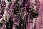 a close-up view of a fabric with a floral pattern, featuring a mix of purple and black colors. The fabric appears to be made of a sheer material, with sequins and beads adding a decorative touch.