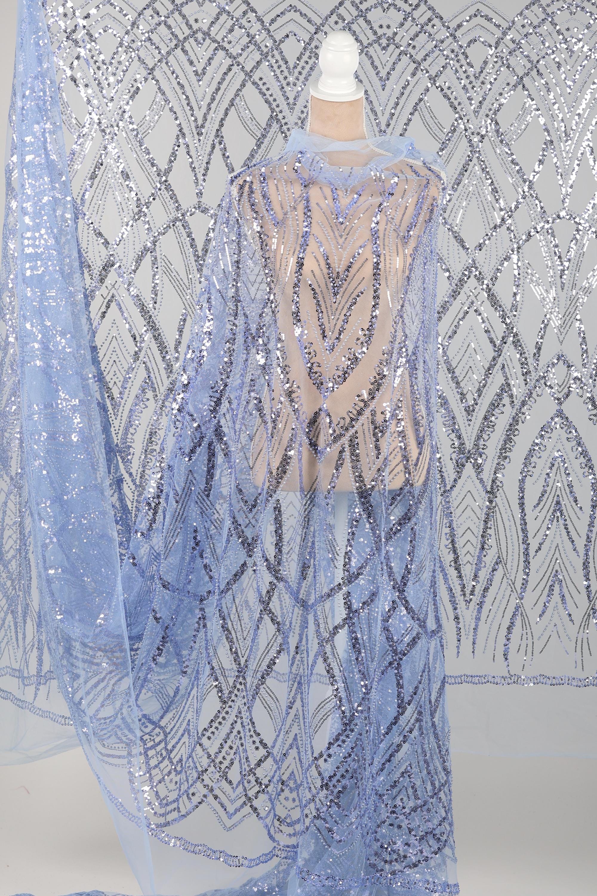 a mannequin wearing a long, flowing blue sequin cape. The cape has a pattern of geometric shapes and lines, creating a visually striking and intricate design. The mannequin is positioned in front of a background with a similar pattern of sequin designs, creating a cohesive and visually appealing display.