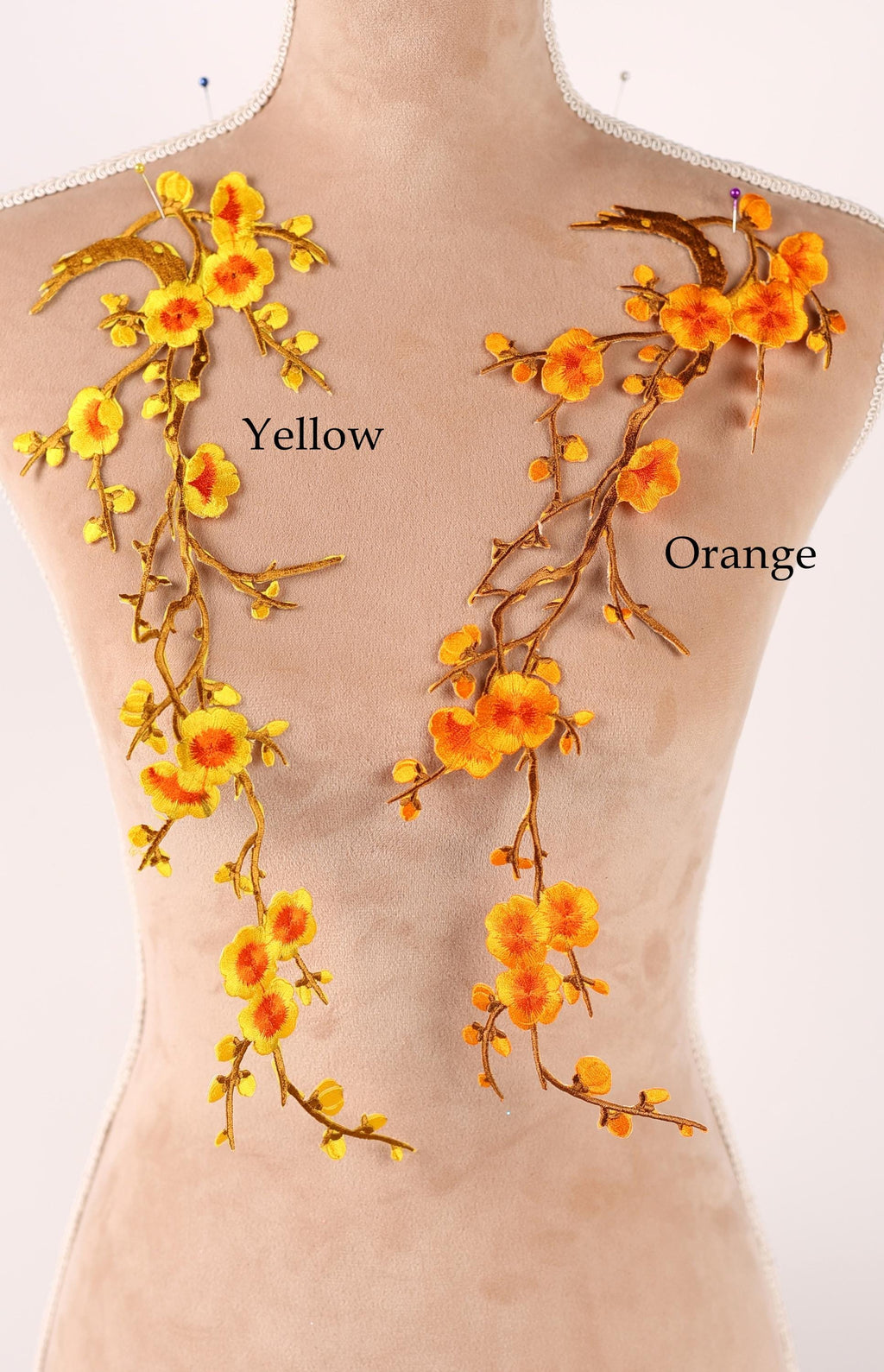 a mannequin with two distinct floral designs on its torso. The left side of the mannequin has yellow flowers, while the right side has orange flowers. The flowers are attached to the mannequin using embroidery techniques, creating a visually striking contrast between the two floral designs.