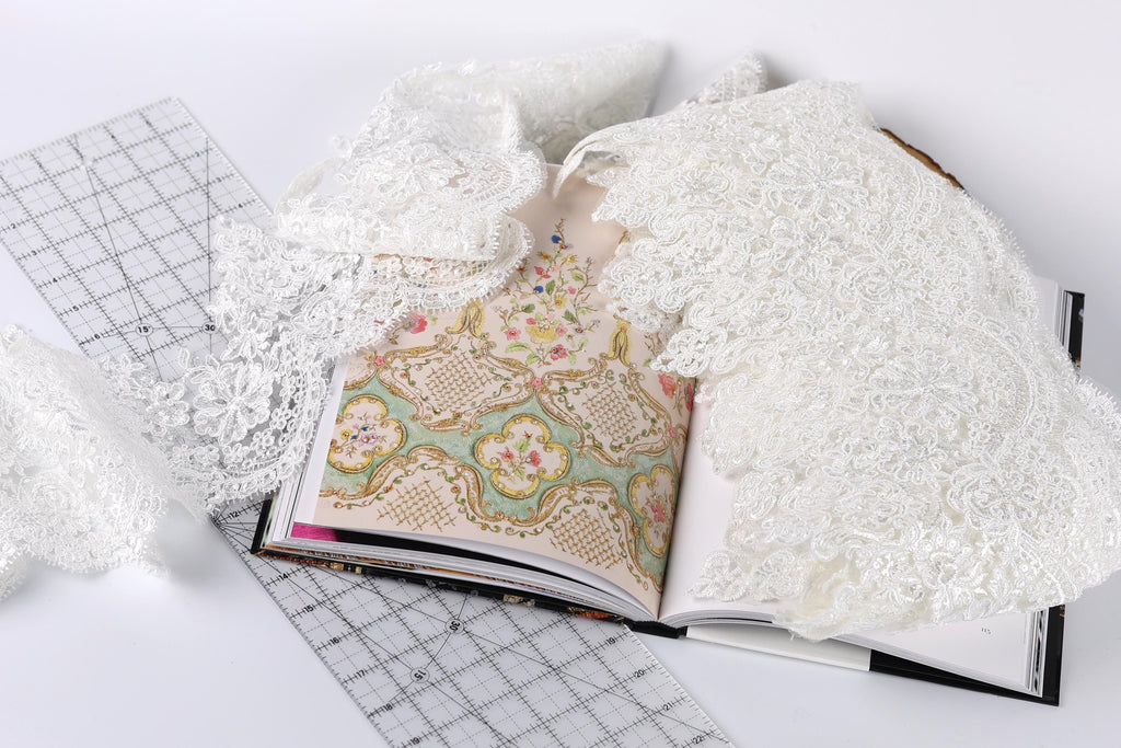 an open book with a lace pattern on the cover, along with a ruler and some white lace fabric.