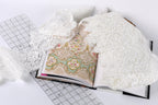 an open book with a lace pattern on the cover, along with a ruler and some white lace fabric.