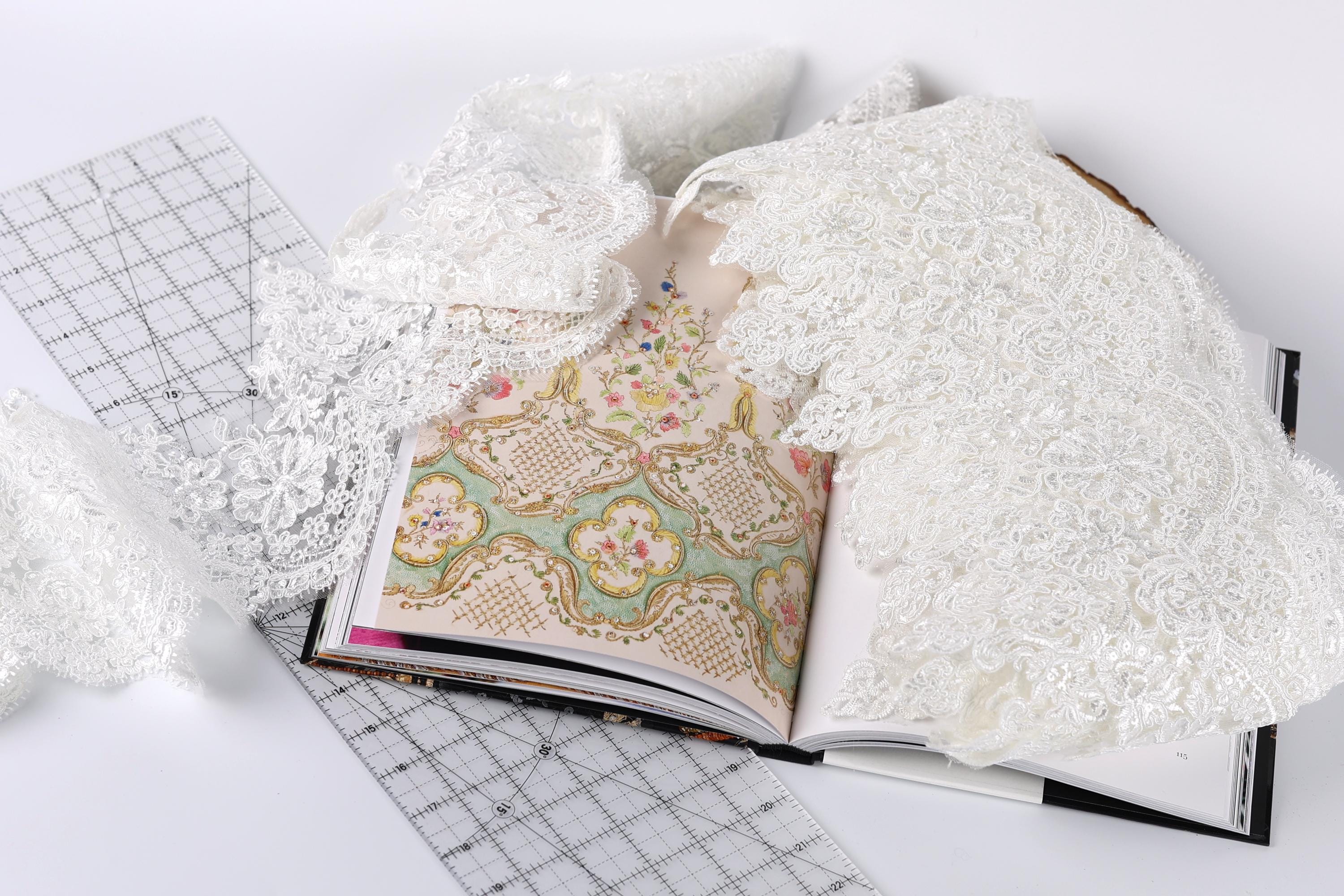 an open book with a lace pattern on the cover, along with a ruler and some white lace fabric.