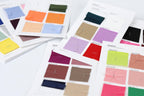 a collection of fabric swatches, each with a different color, arranged on a white background. The swatches are spread out, with some overlapping each other, creating a visually interesting display of various colors and patterns.