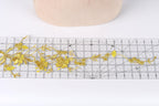 a close-up view of a piece of fabric with gold embroidered flowers, placed on a ruler for scale.