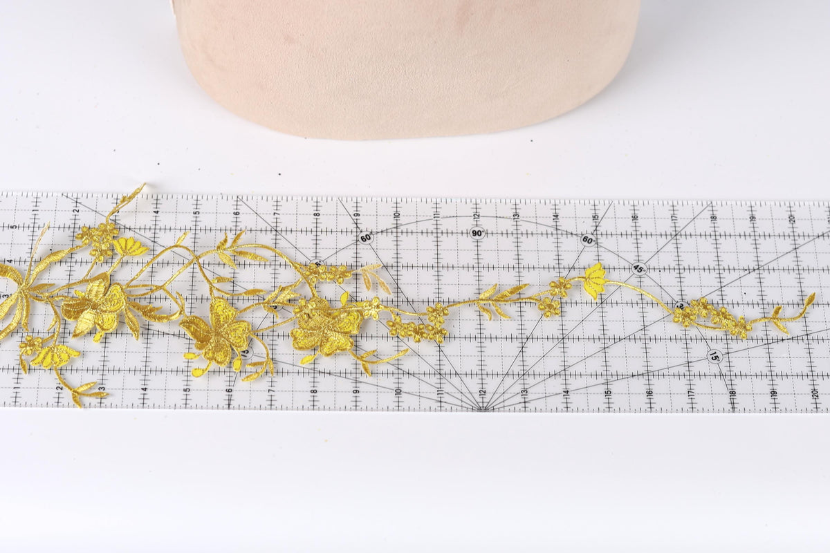 a close-up view of a piece of fabric with gold embroidered flowers, placed on a ruler for scale.