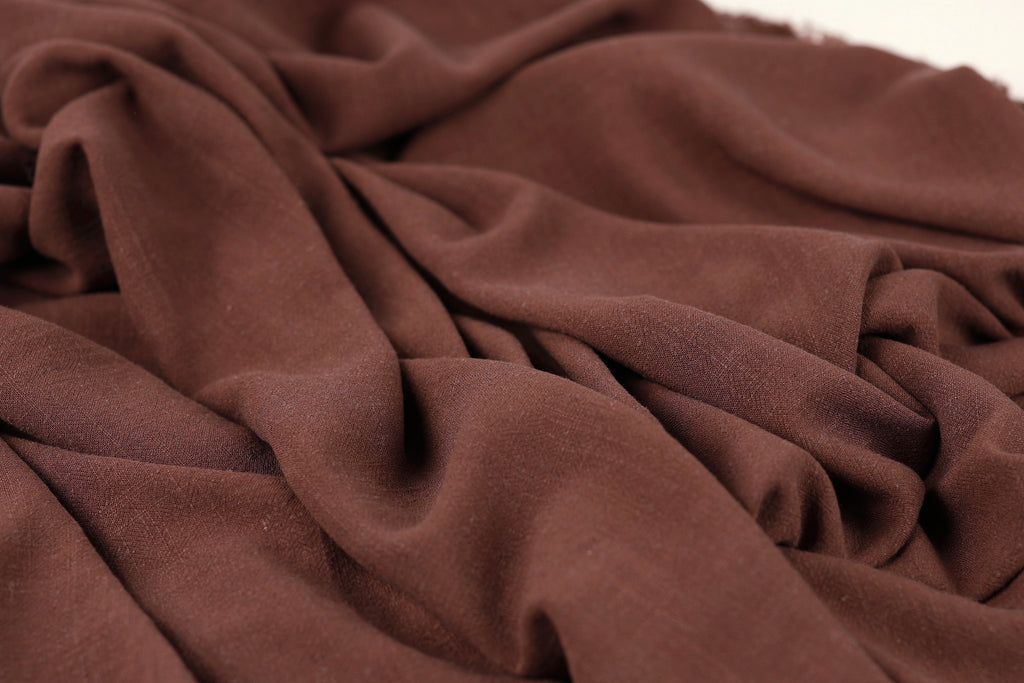 A close-up view of a brown fabric, possibly a piece of clothing or textile, with a crumpled and wrinkled texture.