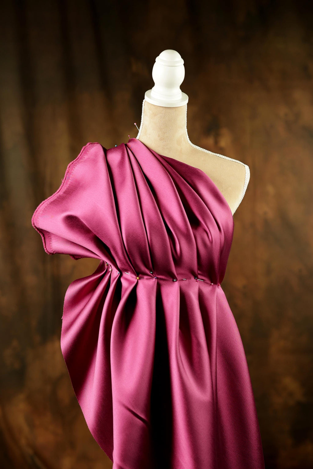 A mannequin wearing a vibrant, one-shoulder pink satin dress with a ruched waist and a draped skirt.
