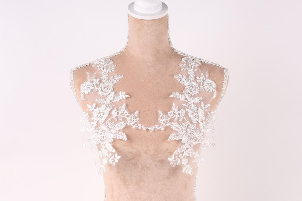 A mannequin with a white lace bodice and a white lace overlay, showcasing intricate floral patterns.