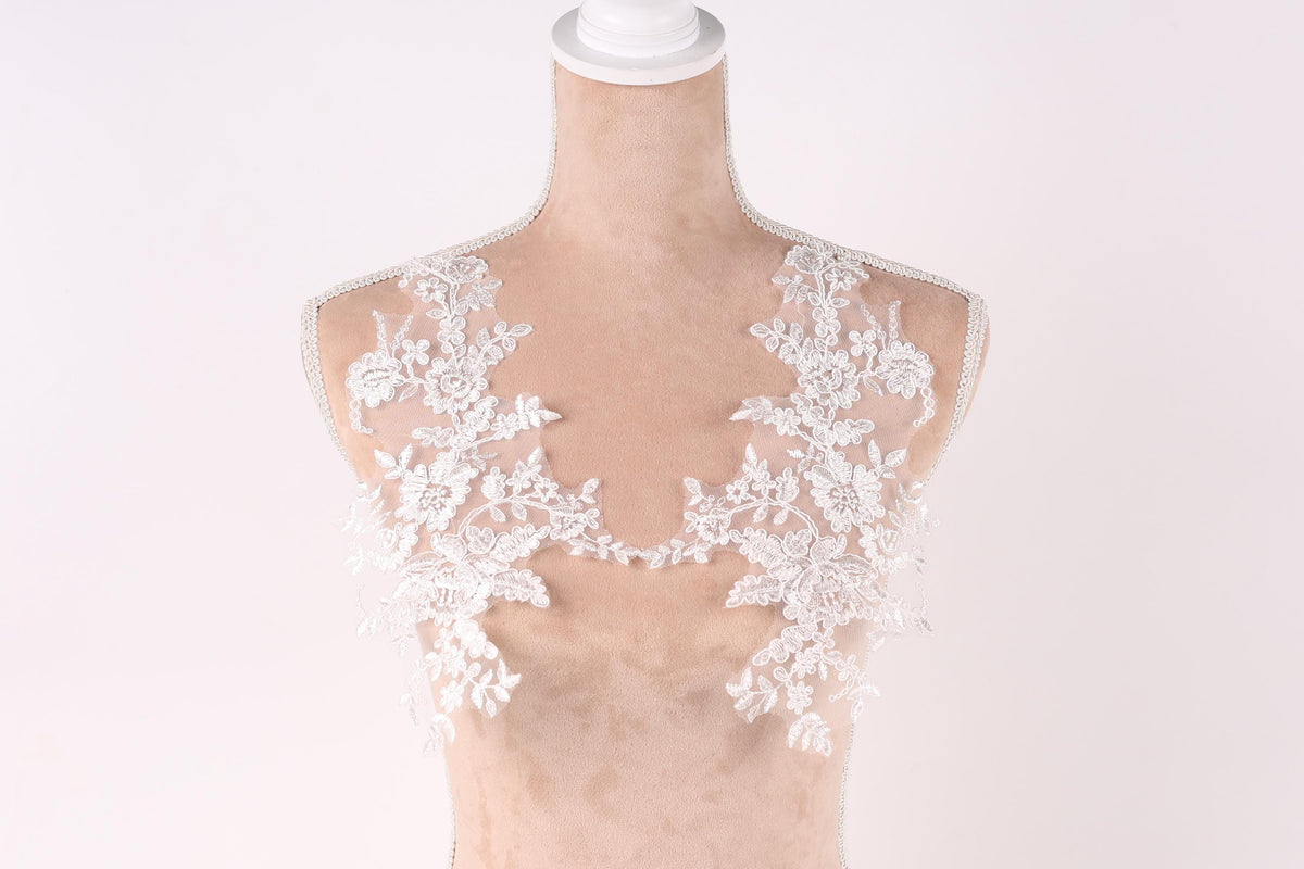 A mannequin with a white lace bodice and a white lace overlay, showcasing intricate floral patterns.
