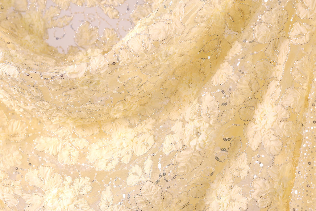 The image is a close-up of a fabric with a yellow floral pattern, featuring small white flowers and silver sequins.