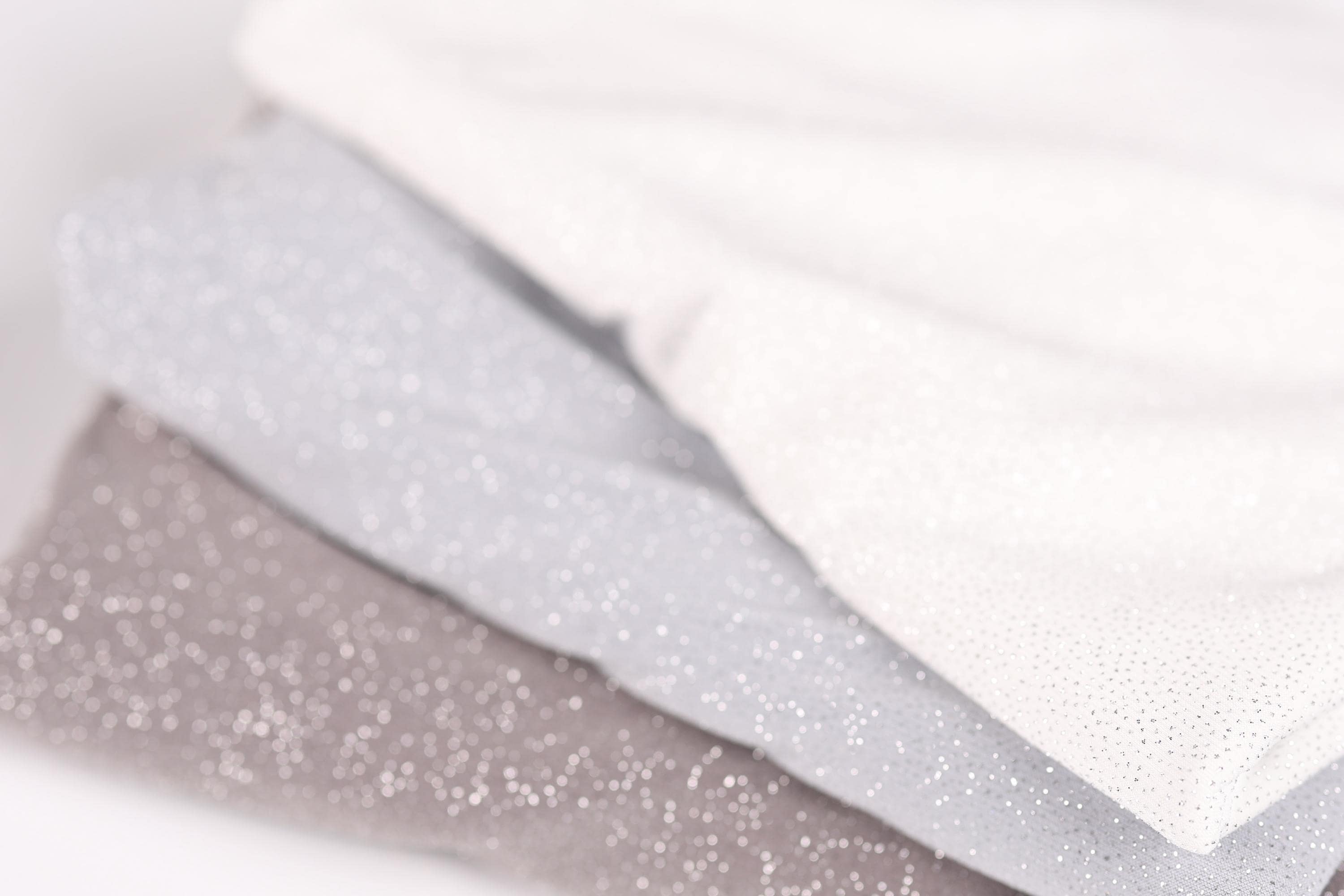 A close-up image of three fabric swatches, with a focus on the middle one, which appears to be a light gray fabric with a sparkly texture.