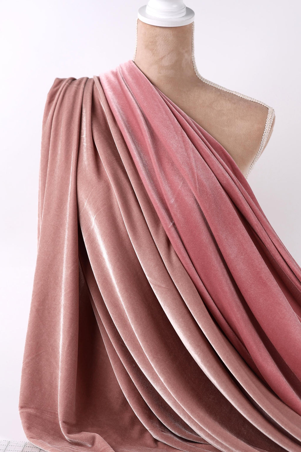 A mannequin wearing a pink velvet dress with a draped, flowing fabric draped over its shoulder.