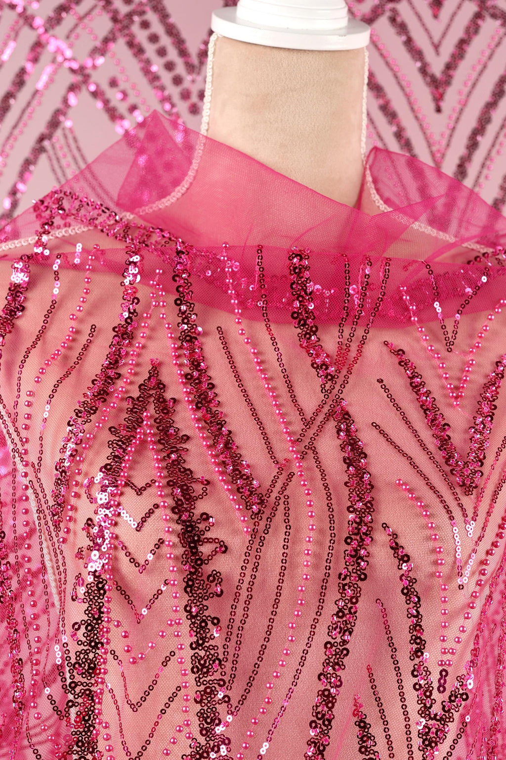 a mannequin wearing a pink sequin dress with a pink collar. The dress has a pink and black patterned design, and the sequin details are visible throughout the fabric.