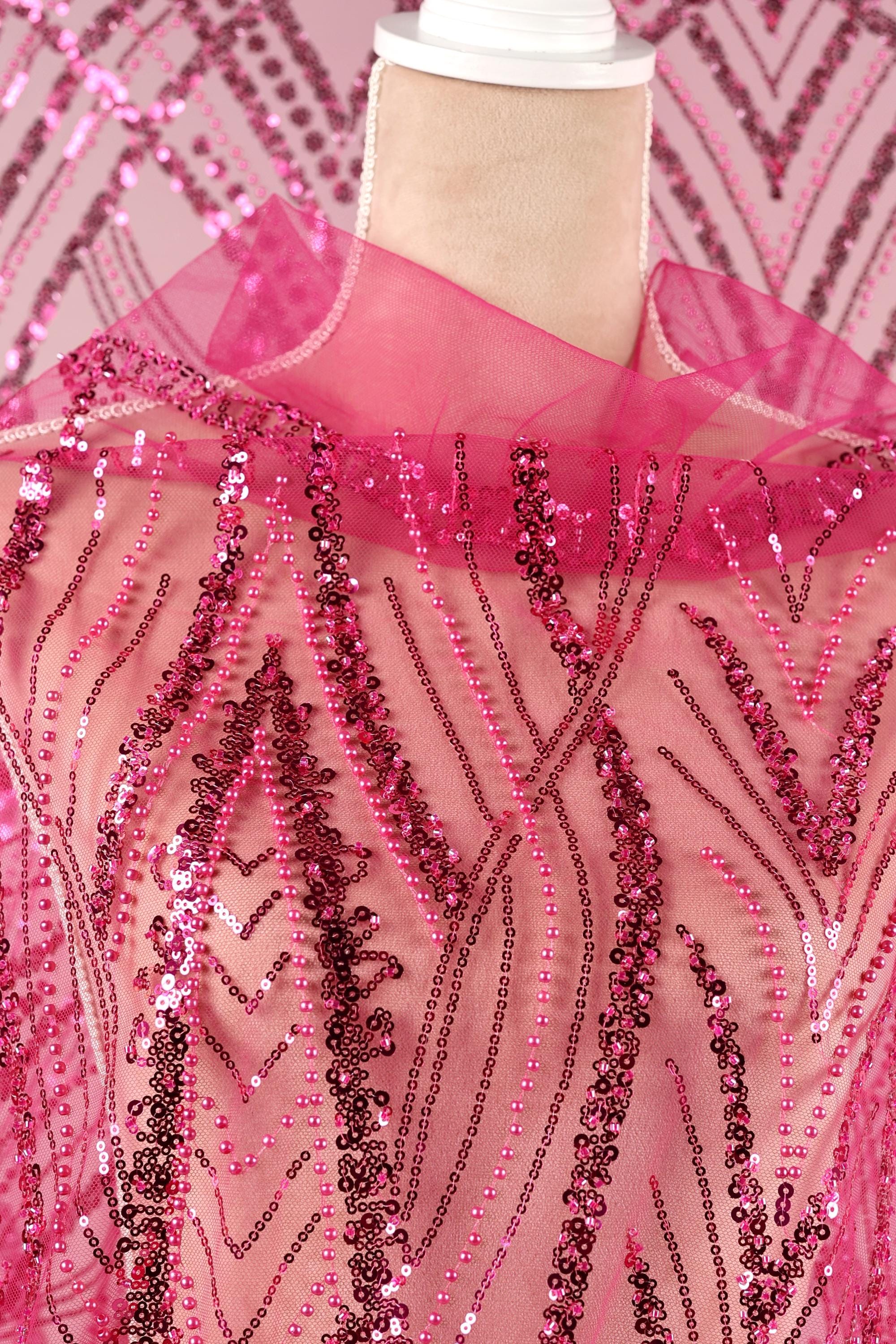 a mannequin wearing a pink sequin dress with a pink collar. The dress has a pink and black patterned design, and the sequin details are visible throughout the fabric.