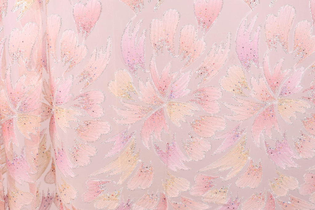 a close-up view of a fabric with a repeating pattern of pink and white flowers or leaves. The pattern is intricate and detailed, with the flowers or leaves appearing to overlap and create a sense of depth and movement. The fabric has a soft, delicate appearance, and the pink and white colors create a harmonious and visually appealing design.