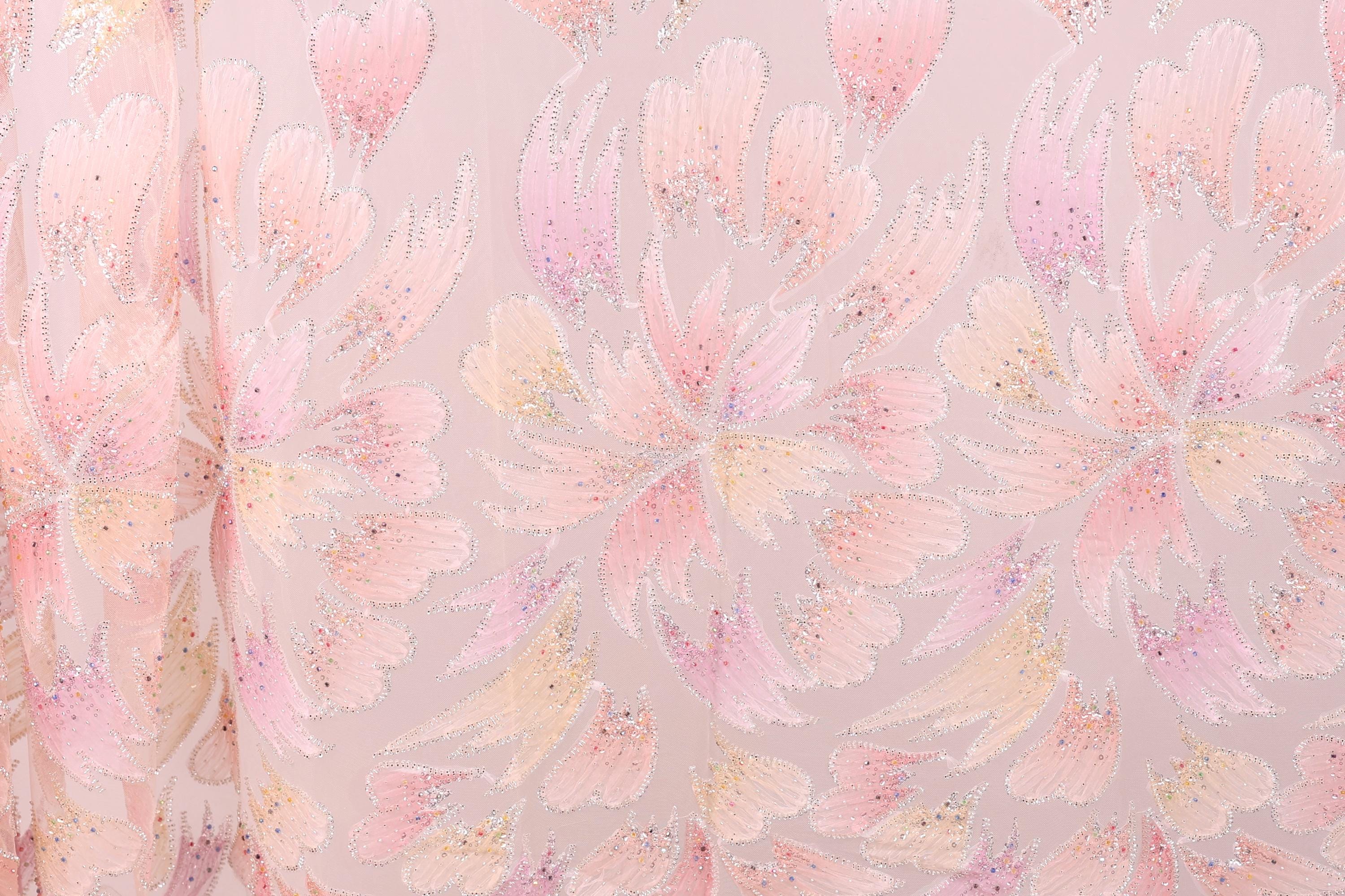 a close-up view of a fabric with a repeating pattern of pink and white flowers or leaves. The pattern is intricate and detailed, with the flowers or leaves appearing to overlap and create a sense of depth and movement. The fabric has a soft, delicate appearance, and the pink and white colors create a harmonious and visually appealing design.