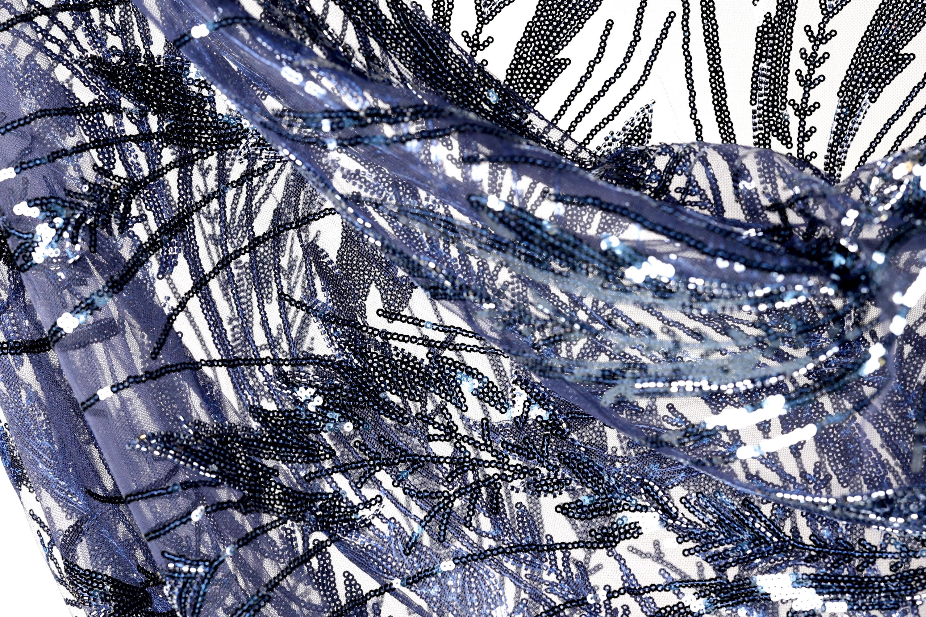 The image is a close-up view of a fabric with a pattern of blue and black sequins, creating a visually striking and intricate design.
