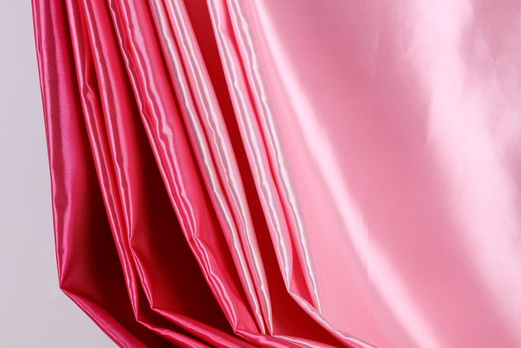 A close-up view of a pink satin fabric, with a soft, flowing texture.