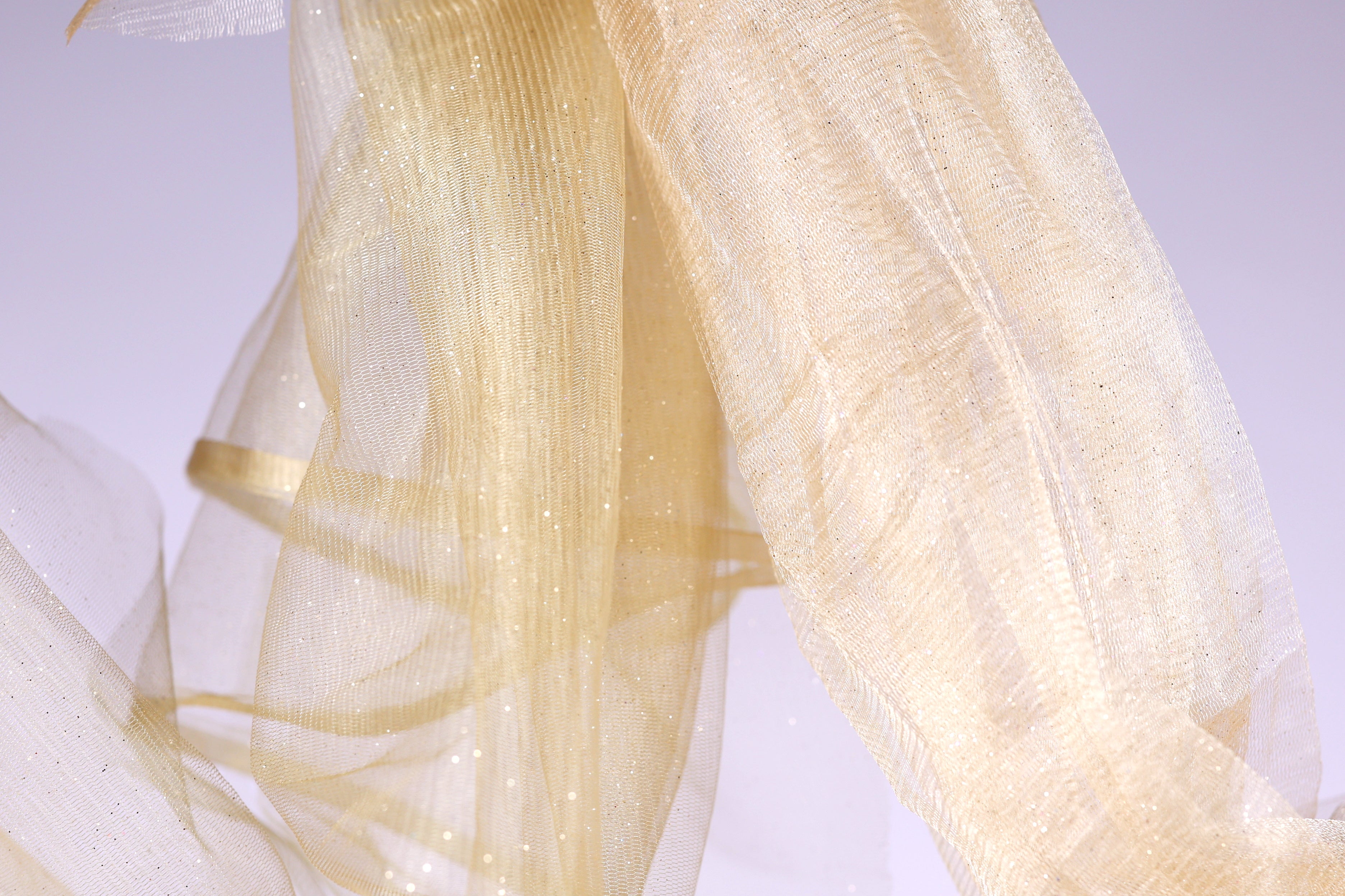 a close-up view of a delicate, shimmering gold fabric, possibly a sheer or sheer-like material, with a soft, flowing texture.