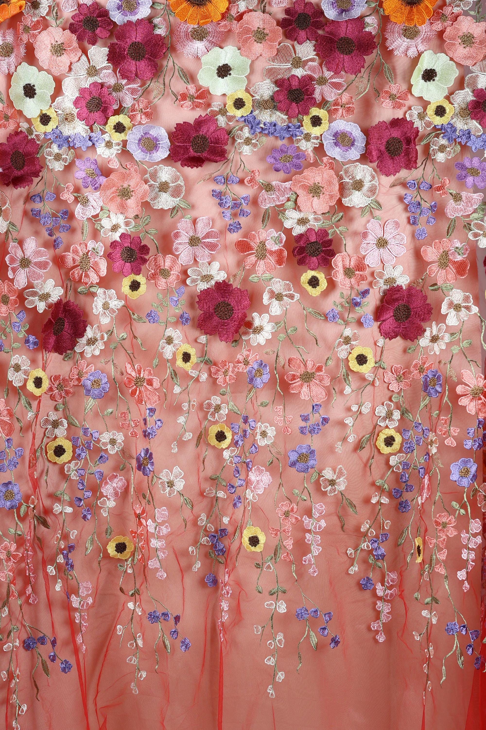a vibrant and colorful floral pattern, with a variety of flowers in shades of pink, purple, yellow, and white. The flowers are intricately embroidered or sewn onto a fabric, creating a visually striking and detailed design.