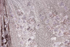 a close-up view of a fabric with a floral pattern, including purple and white flowers and sequins. The fabric appears to be made of a shiny, glittery material, giving it a sparkling and elegant appearance.