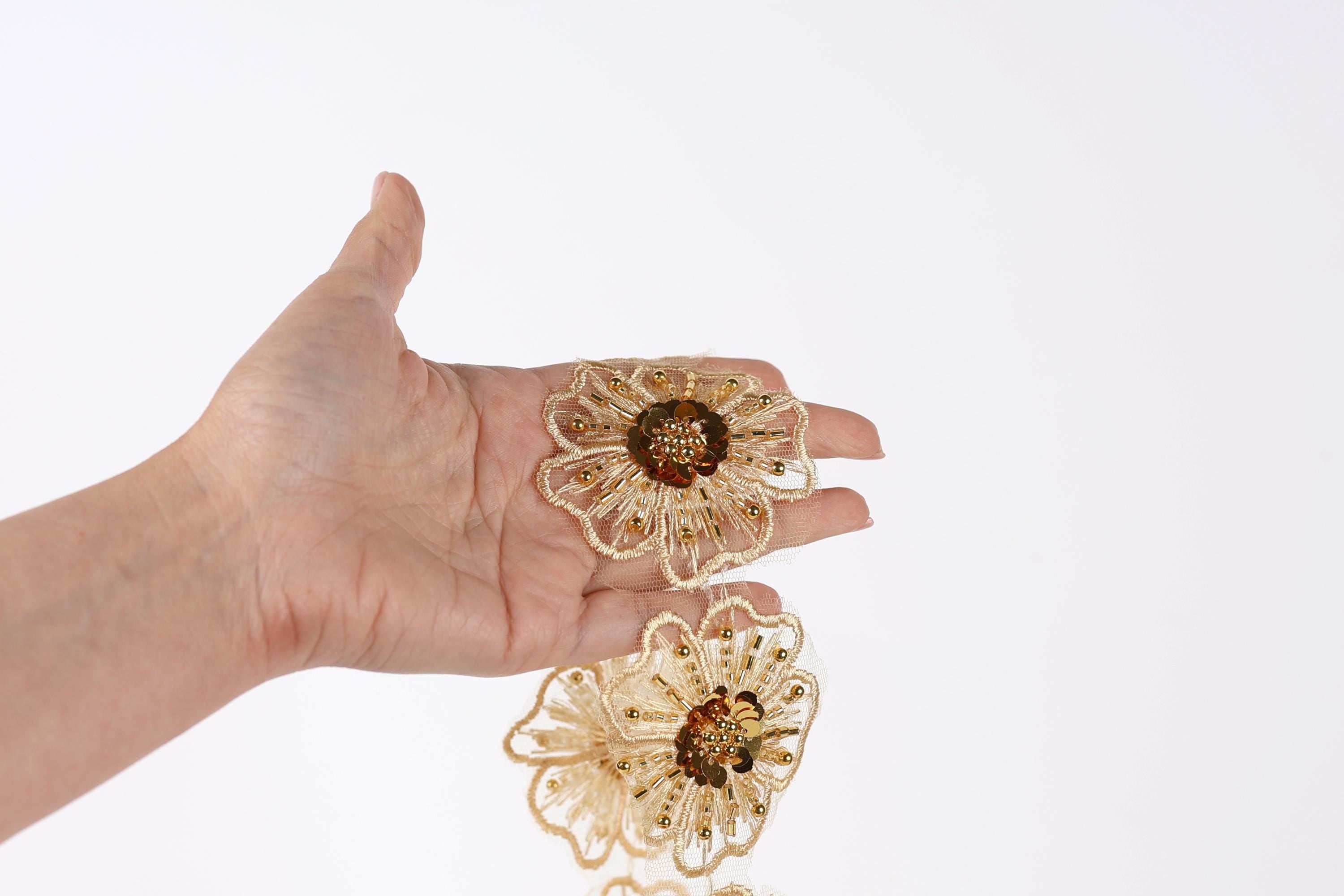 A hand holding two gold flower-shaped earrings against a white background.