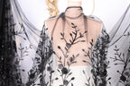 A mannequin wearing a sheer black dress with a floral pattern on the fabric.