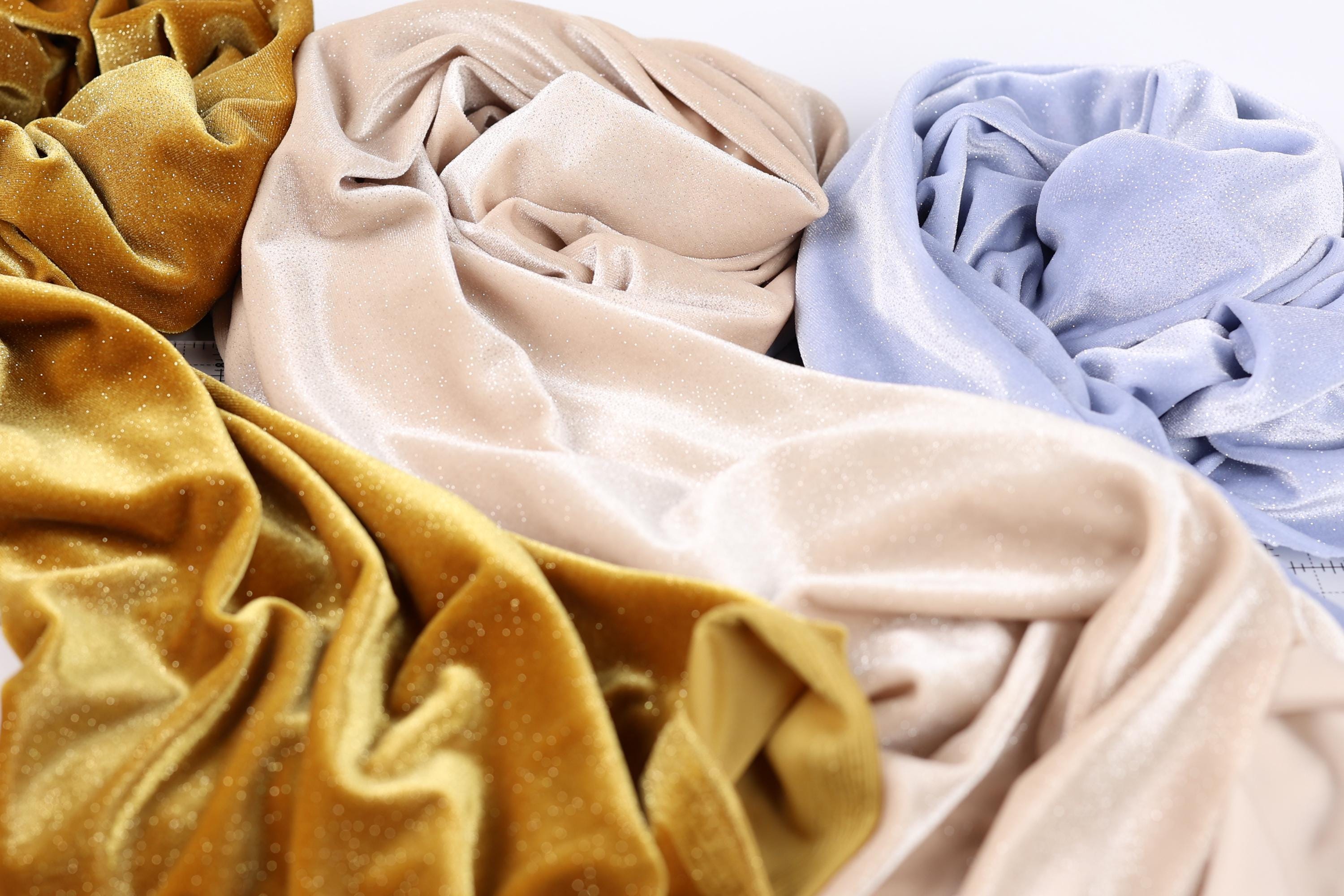 a close-up view of three different fabric swatches, each with a unique color and texture. The fabric appears to be made of velvet, with a shiny, glittery appearance. The swatches are arranged in a way that allows for a clear comparison of their colors and textures.