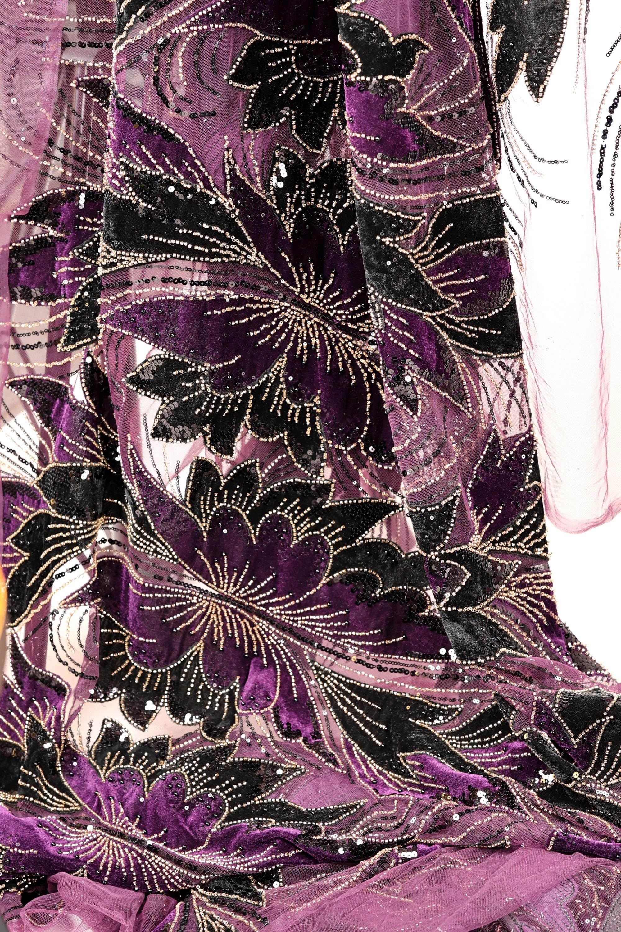 a close-up view of a fabric with a floral pattern in shades of purple and black, adorned with gold embellishments.