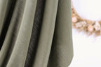 A close-up view of a fabric with a dark stripe running through it, against a blurred background.