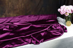 a purple satin fabric draped over a white table, with a vase of pink flowers placed next to it.