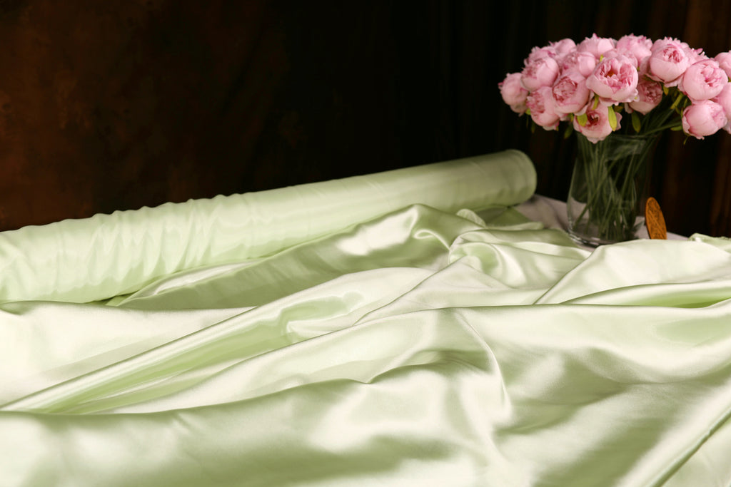 a white satin fabric with a green background, and a vase of pink flowers placed on a table.