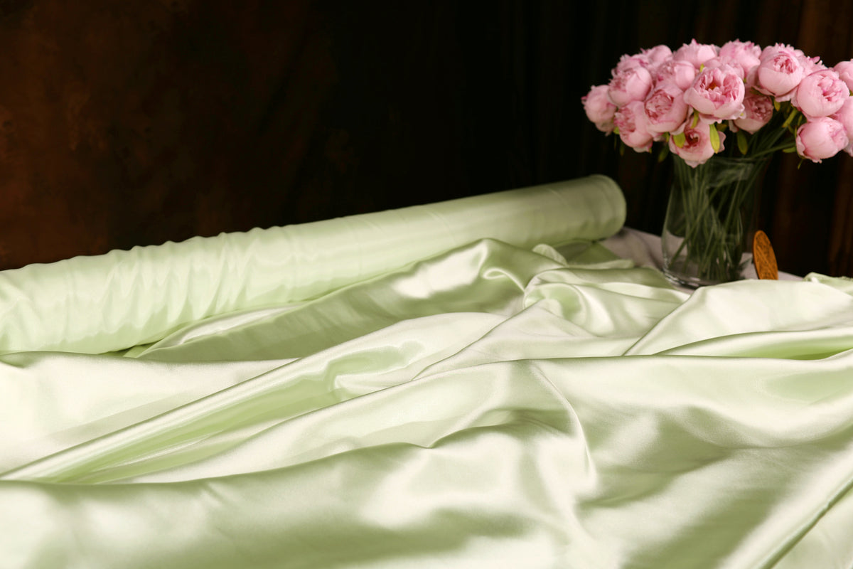a white satin fabric with a green background, and a vase of pink flowers placed on a table.