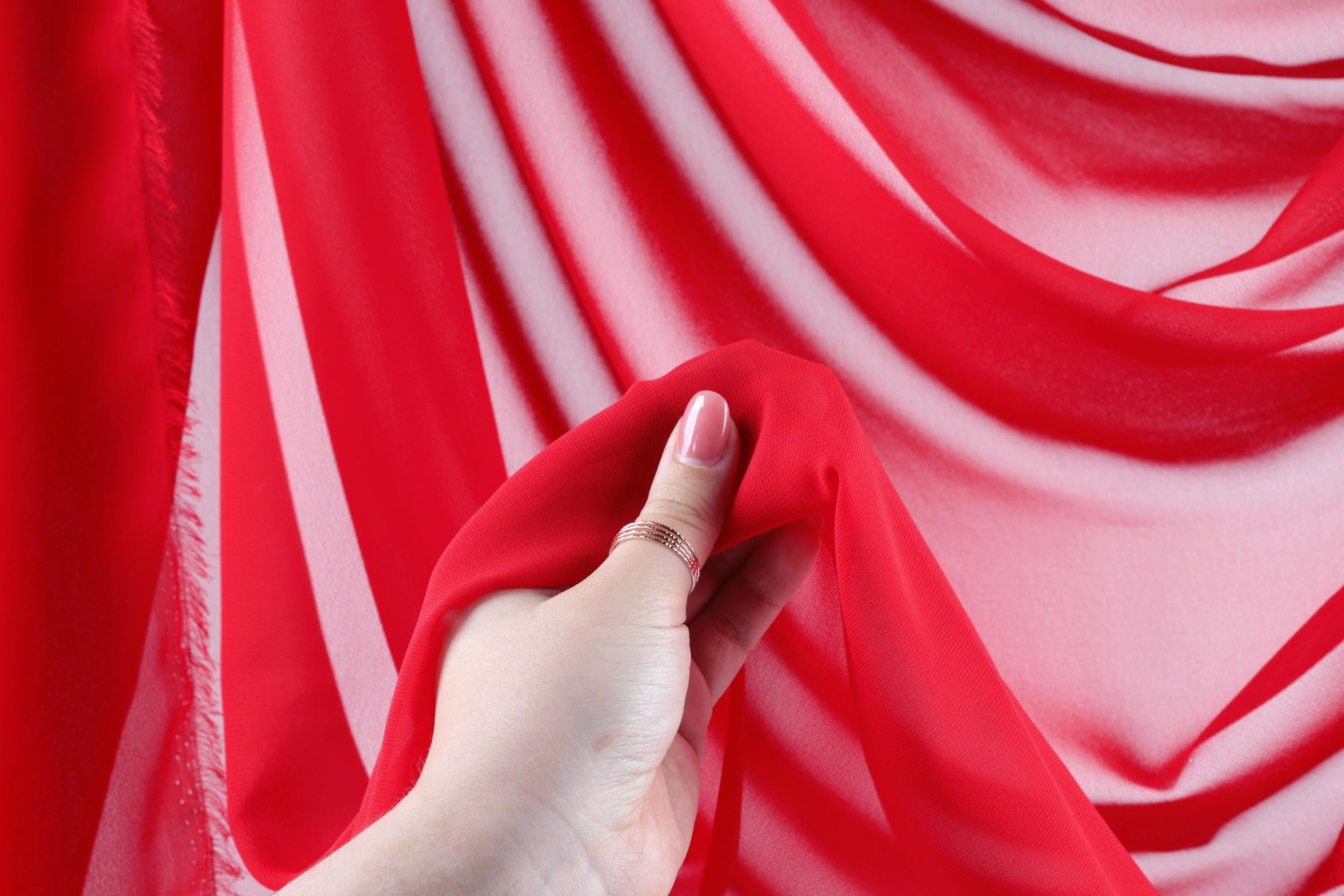 A hand holding a red fabric against a background of red and white fabric.