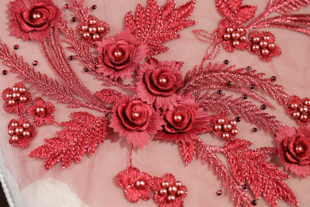a close-up view of a delicate, intricate embroidered design with red flowers and leaves. The design is composed of numerous small red flowers and leaves, creating a visually striking and detailed pattern. The flowers and leaves are arranged in a way that they overlap and interlock, showcasing the skill and craftsmanship of the embroiderer.