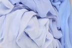 The image is a close-up of a crumpled, light blue fabric, with a blurred background.